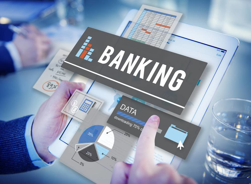 Kotak Mahindra Bank Current Account – Features, Benefits & Online Opening 2025 13 A person interacting with a tablet displaying banking data charts and digital financial icons